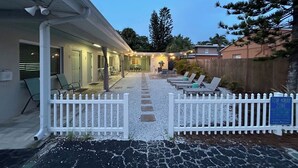 A covered outdoor patio with seating, a white picket fence, and a gravel path leading to a building. - Boutique Stay on Clearwater Beach 1BR Suite w/full Kit
Unit 2 (Clearwater Beach)