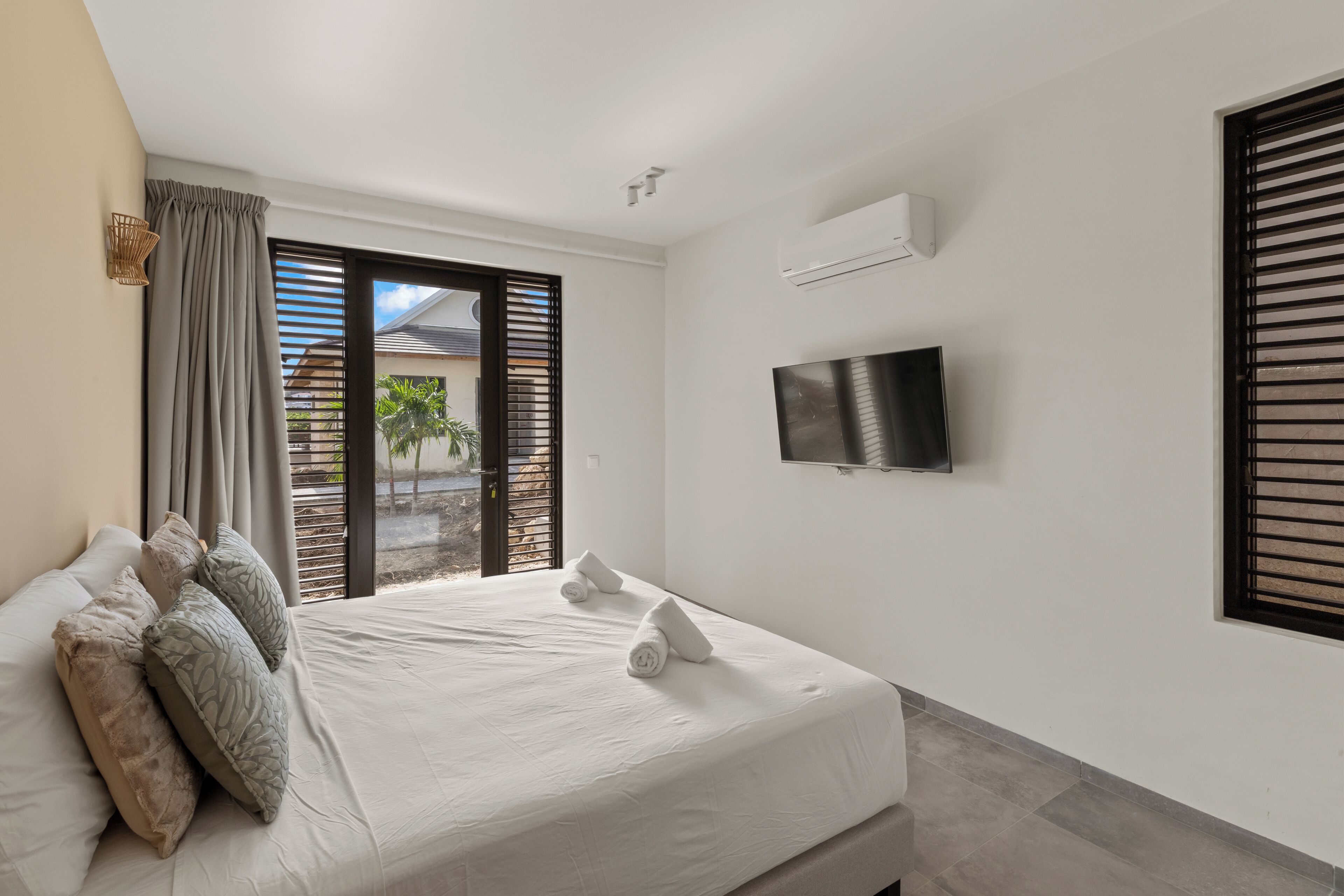 A modern hotel room with a large bed, a flat-screen TV mounted on the wall, and a sliding glass door leading to an outdoor area.