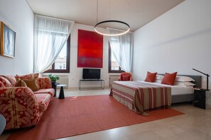 Ein modernes Schlafzimmer mit einer Couch, einem Bett, einem Fernseher und einem großen Fenster.
