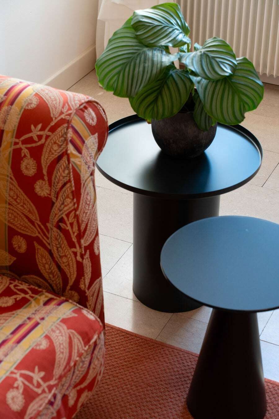 Une pièce avec un canapé rouge à motifs, une petite table ronde, une plante en pot et un radiateur.