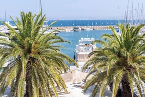 Uma marina com vários barcos atracados, palmeiras ao primeiro plano e uma vista clara do mar.