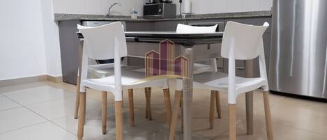 A modern kitchen with white chairs, a stainless steel refrigerator, and a granite countertop.