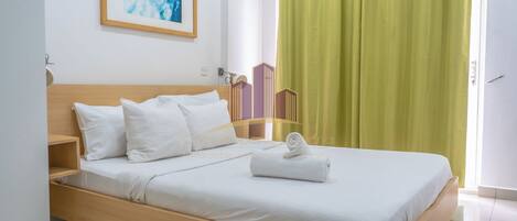 A neatly made bed with white linens and pillows, a wooden headboard, a green curtain, and a framed abstract painting on the wall.