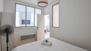 A hotel room with a bed, a standing fan, and a window with a view of the outside. - Bail mobilité - Appart standing proche Vieux-Port (Marseille)