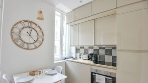 A modern kitchen with white cabinets, a wooden clock, and a dining area with a white table and chairs. - Bail mobilité - Appart standing proche Vieux-Port (Marseille)