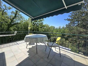 A balcony with a table and chairs, a green awning, and a view of trees. - Holiday apartment for 3 people near the beach (Njivice)