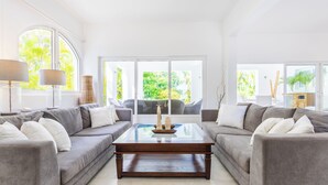 Un salón moderno con dos sofás grises, una mesa de centro de cristal y ventanas amplias que dan a zonas verdes.