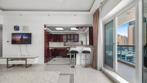 A modern living room with a TV, a dining table, and a kitchen area visible through an open door. - Opal Tower Residences by CEG Group (Dubai)