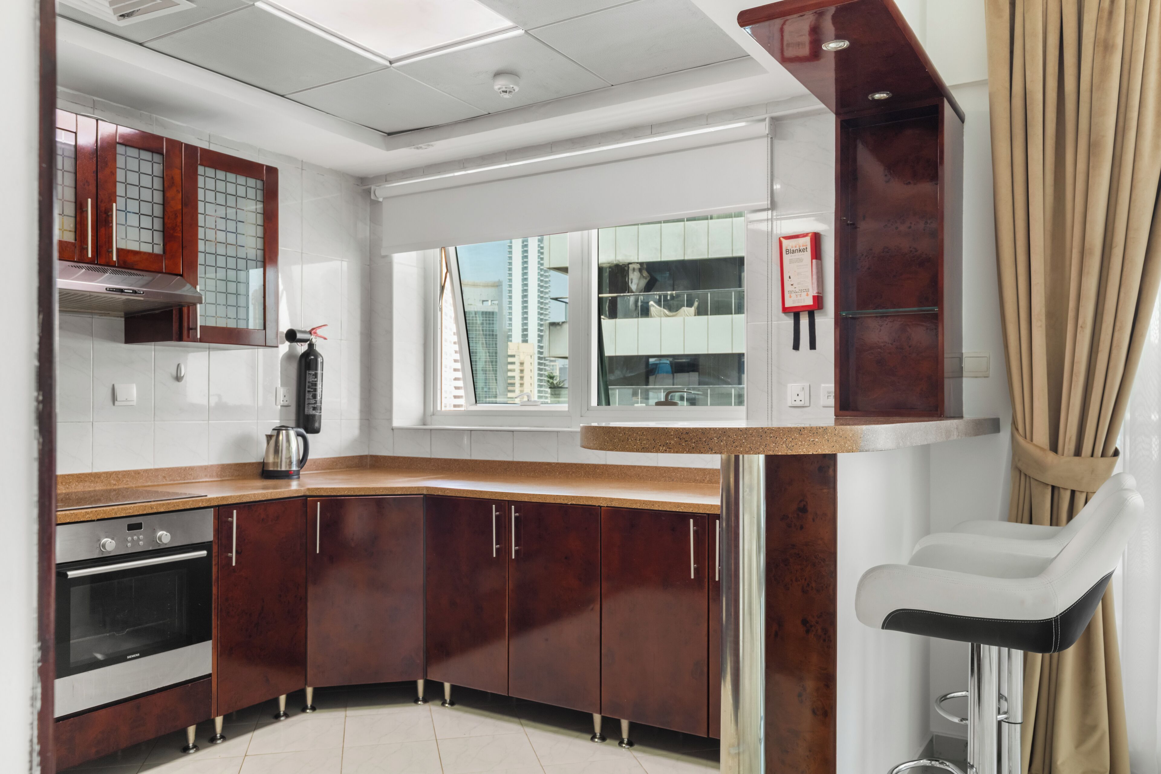 A modern kitchen with a curved countertop, stainless steel appliances, and a window with a city view.