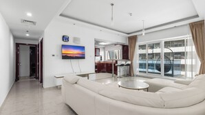 A modern living room with a large sofa, a dining area with high chairs, and a view of a building through large windows. - Opal Tower Residences by CEG Group (Dubai)