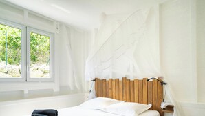 A neatly made bed with white and blue towels, a wooden headboard, and a window with a view of greenery. - Villa Maeva, haven of peace just a few mn walk from the beach & a private pool (Saint-François)