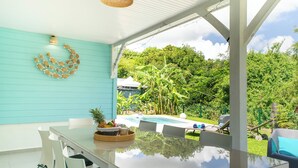 A modern outdoor dining area with a glass table, white chairs, and a view of a swimming pool and lush greenery. - Villa Maeva, haven of peace just a few mn walk from the beach & a private pool (Saint-François)