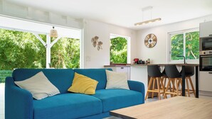 A modern living room with a blue sofa, a wooden coffee table, and a kitchen area with a sink, stove, and bar stools. - Villa Maeva, haven of peace just a few mn walk from the beach & a private pool (Saint-François)