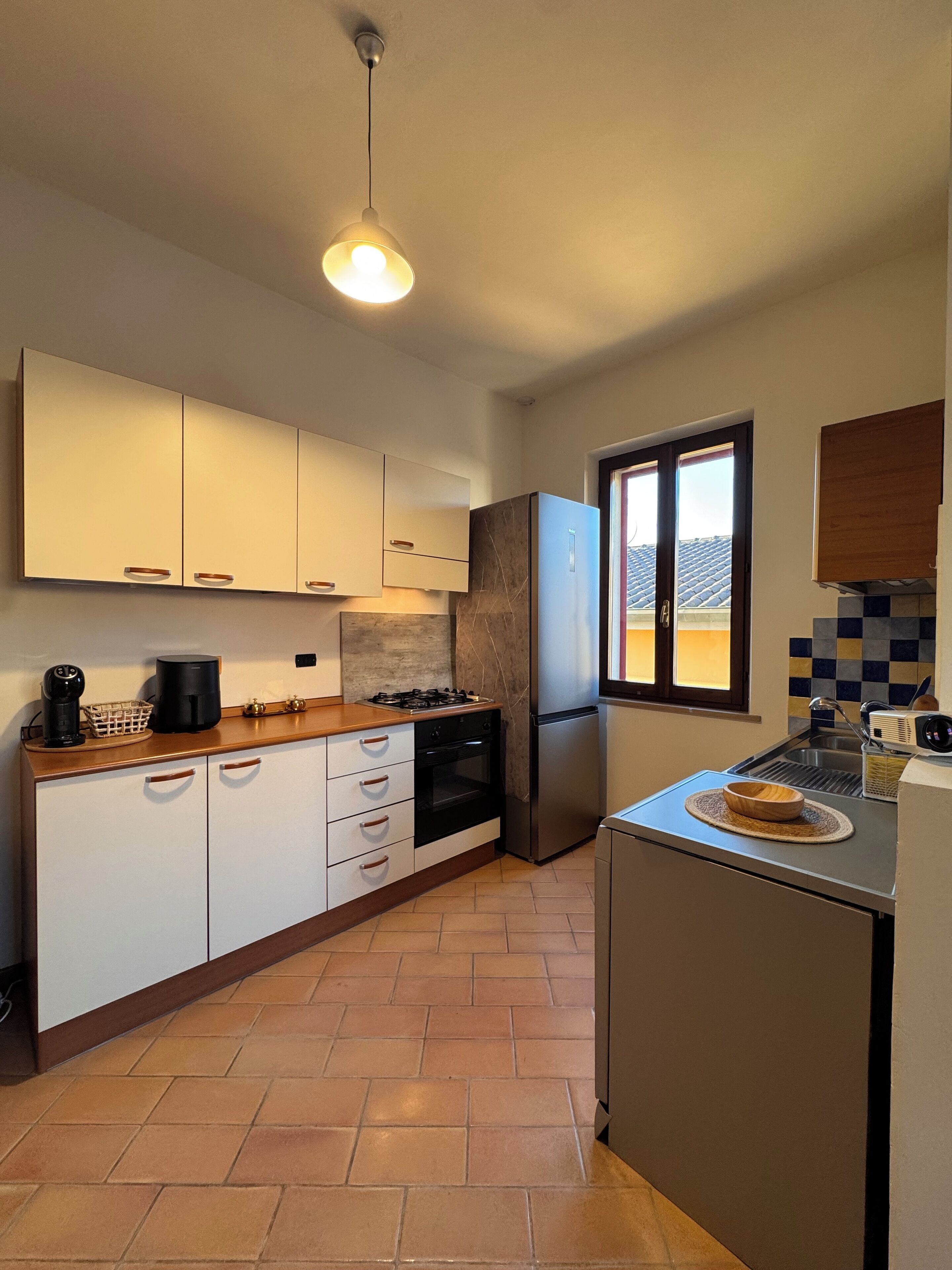 A modern kitchen with white cabinets, a stainless steel refrigerator, a gas stove, and a window providing natural light.