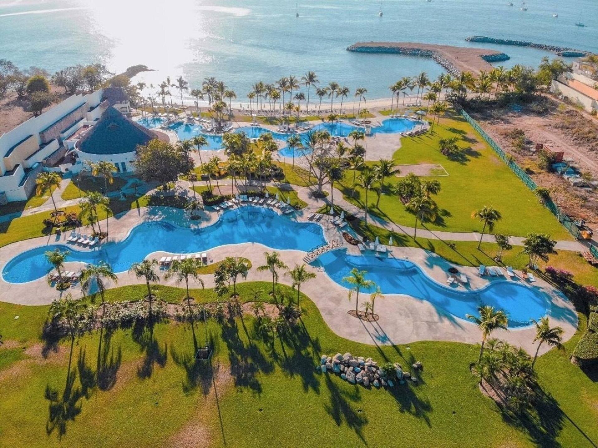 Vista aérea de un resort con varias piscinas, palmeras y una zona de playa.