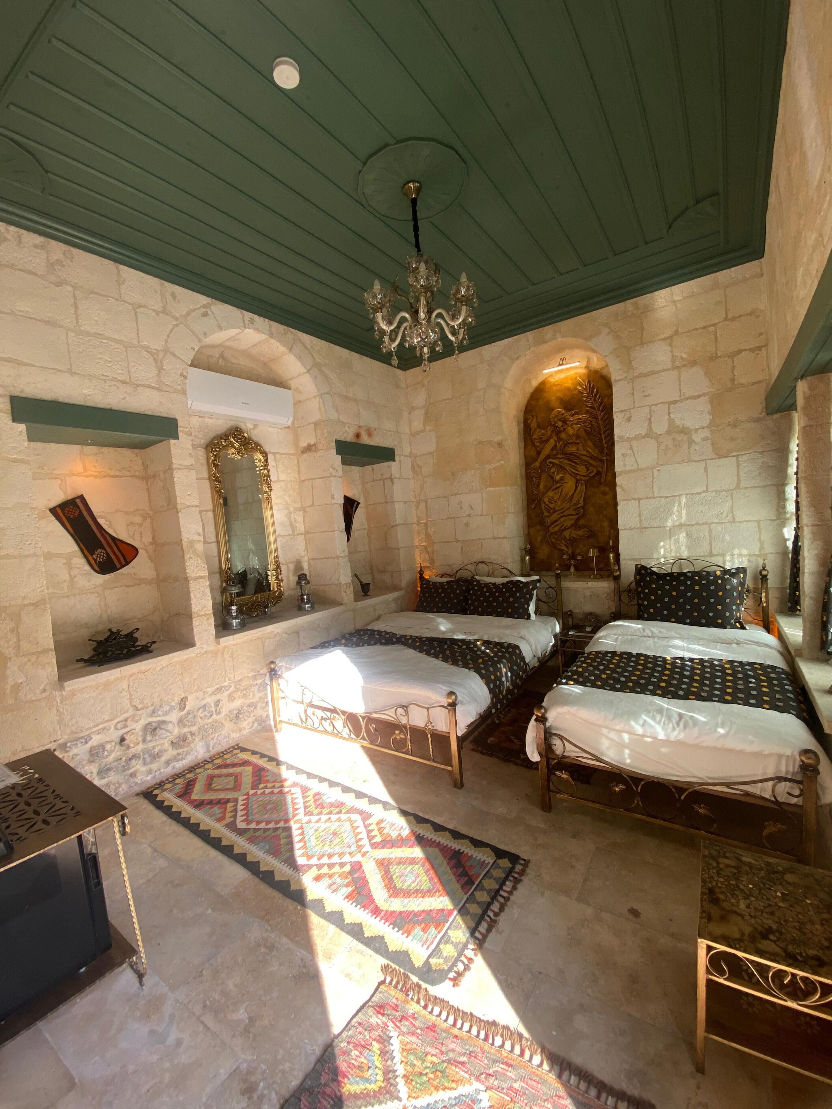 A room with a stone wall, a chandelier, a bed with patterned bedding, and a rug.