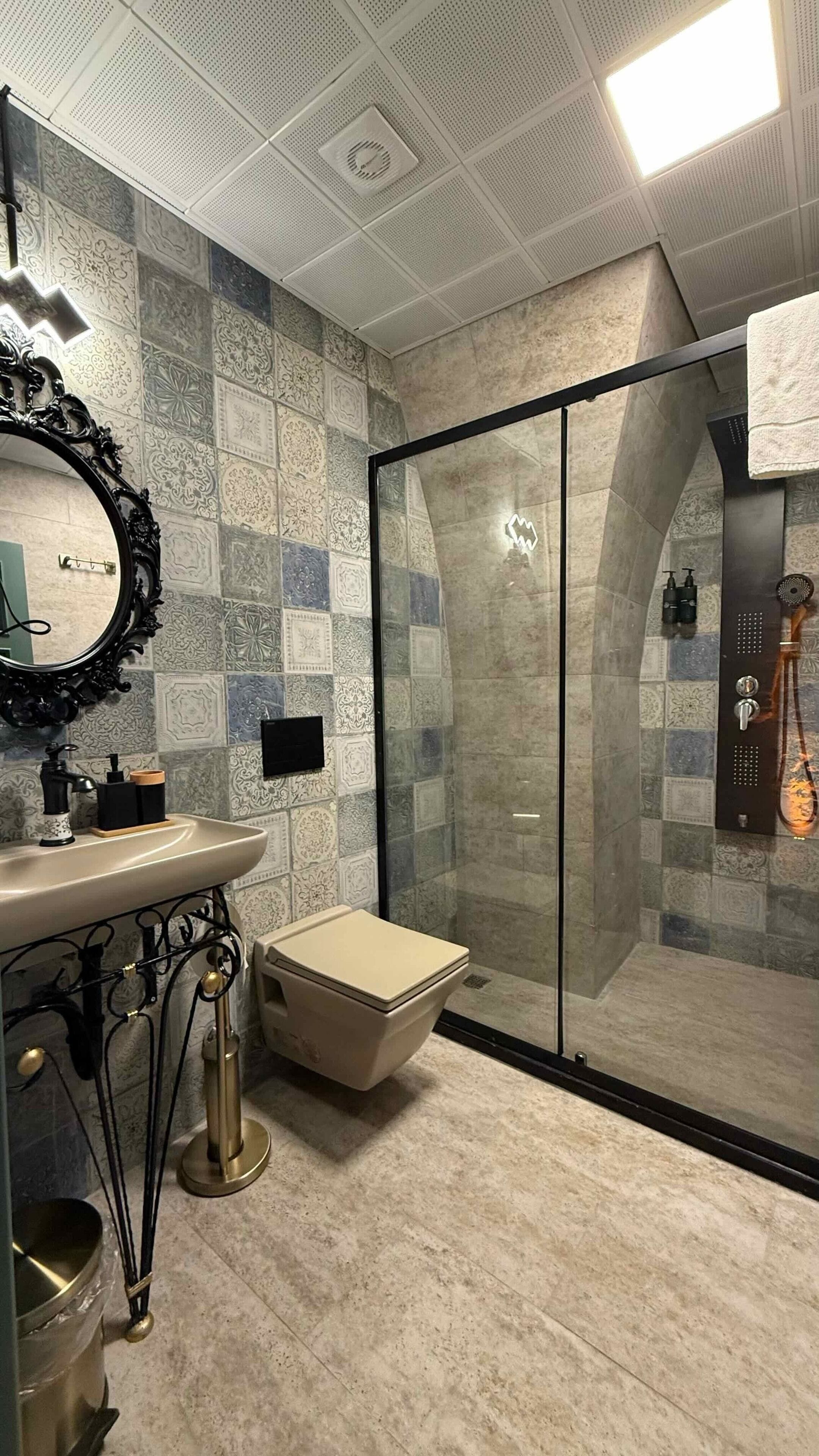 A bathroom with a tiled backsplash, a sink with a mirror, a toilet, and a glass-enclosed shower area.