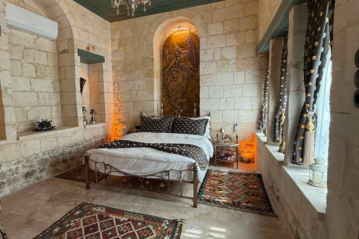 Une chambre aux murs de pierre, comprenant un lit, une table de chevet, un élément décoratif mural et une fenêtre avec des rideaux.