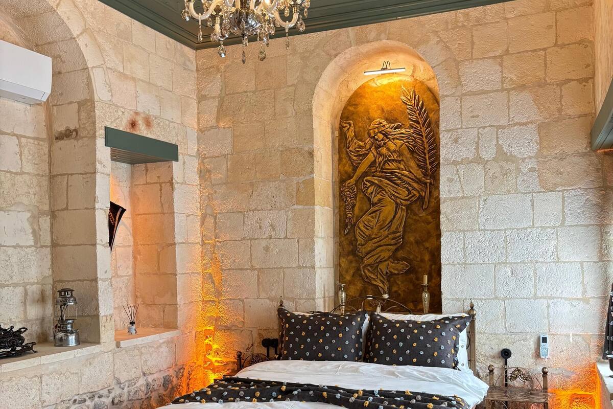 Une chambre avec un mur en pierre, un lustre, un lit avec une literie à motifs et un élément décoratif mural.