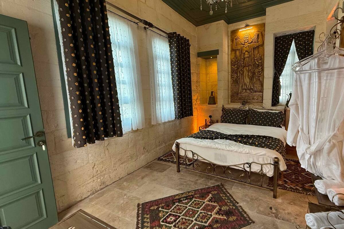 Une pièce avec un lit, un fauteuil suspendu, un tapis à motifs et une porte verte.