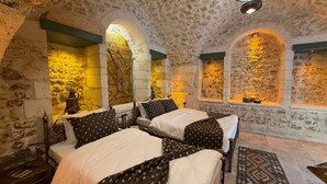 A room with stone walls, two beds with patterned bedding, and a patterned rug on the floor. - Liora Hotel (Şanlıurfa)
