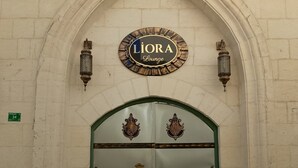 En dubbeldörr med en grön ram och utsmyckade metallhandtag, placerad under en spetsbågig portal med en skylt som visar texten "Liora Lounge".