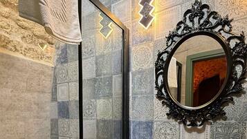 A bathroom with a glass shower door, a sink with a decorative mirror, and patterned tiles on the walls.