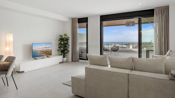 A modern living room with a large window, a flat-screen TV, a sofa, and a dining area. - Venían Views 2BR Selwo Estepona (Málaga)