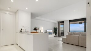 A modern living space with a kitchen island, a sofa set, and a large window offering a view of the sea. - Venían Views 2BR Selwo Estepona (Málaga)