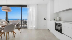 A modern kitchen with white cabinets, a built-in oven, and a dining area with a table and chairs. - Higueron Sea View Penthouse 2BR (Fuengirola)