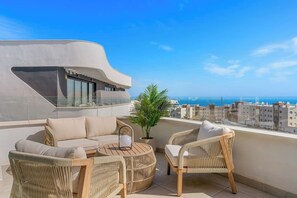 A rooftop terrace with a curved white wall, wicker furniture, and a view of the sea and cityscape. - Higueron Penthouse with Ocean View, 2 Bedrooms (Fuengirola)