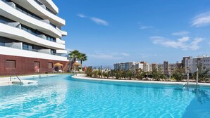A swimming pool with a clear blue water, surrounded by a modern building with multiple balconies and a view of other buildings in the background. - Higueron Sea View Penthouse 2BR (Fuengirola)