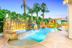 A pool area with a waterfall, palm trees, and a slide. - Lights, Camera, Vacation! (Indio)