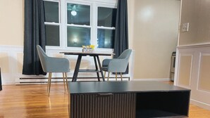 Un saló modern amb una taula de centre de fusta fosca, dues cadires grises i una finestra amb cortines negres.