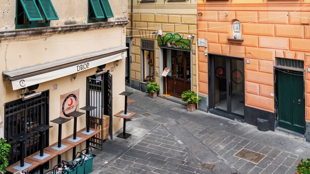 Une rue étroite bordée d’immeubles aux volets verts et d’un magasin dont l’enseigne indique « DROP ».