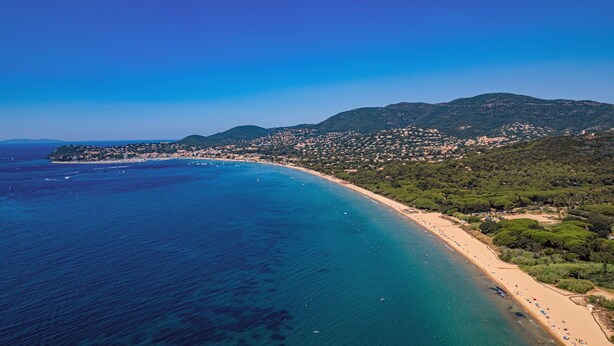 An aerial view of a coastal town with a beach, clear blue sea, and hilly background. - Apartment 'Petit Paradis' with Shared Pool, Wi-Fi, and Air Conditioning (Cavalaire-sur-Mer)