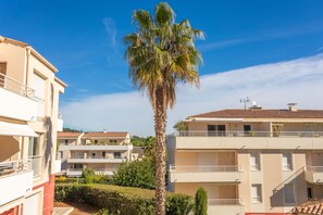 A multi-story building with balconies, a palm tree, and a clear blue sky.