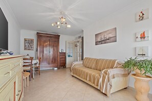 A living room with a sofa, a dining table with chairs, a wooden cabinet, and a ceiling light fixture.
