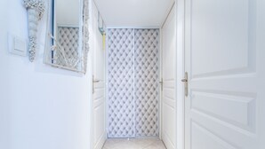 A hallway with white walls, a mirrored wall, a door with a white panel, and a tiled floor. - Apartment 'Petit Paradis' with Shared Pool, Wi-Fi, and Air Conditioning (Cavalaire-sur-Mer)