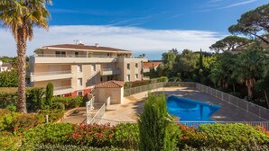A multi-story building with a swimming pool, surrounded by greenery and palm trees. - Apartment 'Petit Paradis' with Shared Pool, Wi-Fi, and Air Conditioning (Cavalaire-sur-Mer)