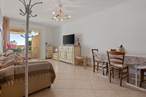 A room with a bed, a dining table with chairs, a television, and a chandelier.