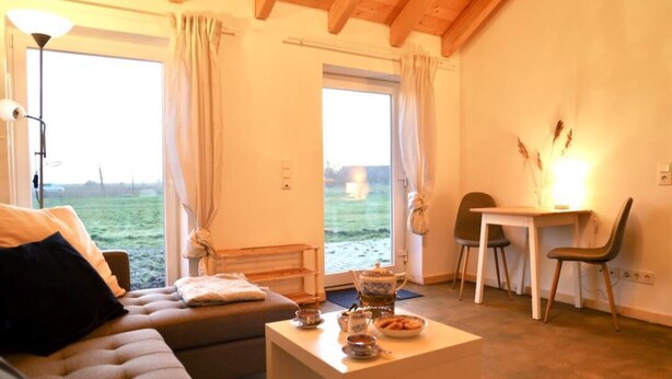 Un salón acogedor con un sofá, una mesa de centro con juego de té, y vistas a un campo verde a través de un ventanal grande.