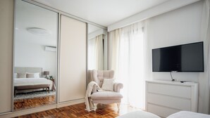Een moderne hotelkamer met een grote spiegel, een bed, een stoel, een televisie en een houten vloer.