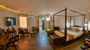 Un lit à baldaquin, une télévision, un bureau et une chaise dans une pièce au plancher en bois et aux murs blancs.
