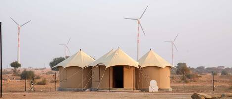 A desert landscape with three tents and wind turbines in the background.