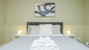 A neatly made bed with white linens and towels, two bedside lamps, and a large abstract painting on the wall. - 2BR Trafalgar Retreat near UBC & Pacific Spirit (Vancouver)