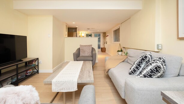 A modern living room with a flat-screen TV, a grey sofa, a wooden coffee table, and a grey armchair. - 2BR Trafalgar Retreat near UBC & Pacific Spirit (Vancouver)
