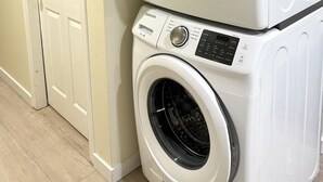A stacked washer and dryer unit in a hallway with a white door and light-colored walls. - 2BR Trafalgar Retreat near UBC & Pacific Spirit (Vancouver)