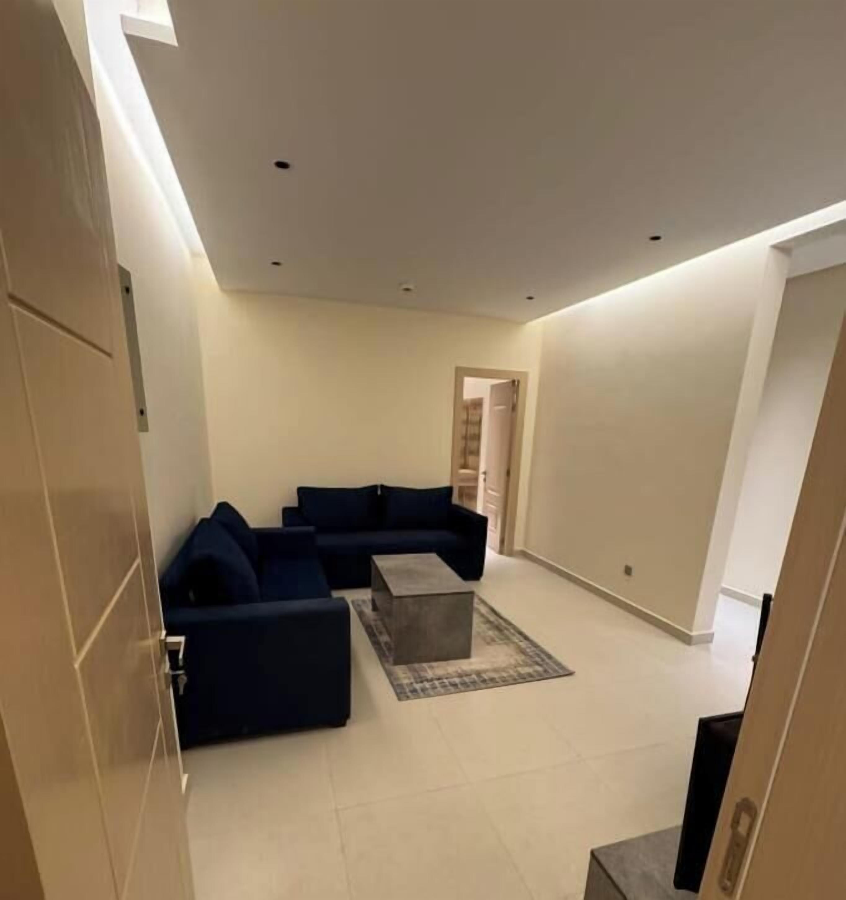 A modern living room with a dark blue sofa set, a coffee table, and a flat-screen TV.