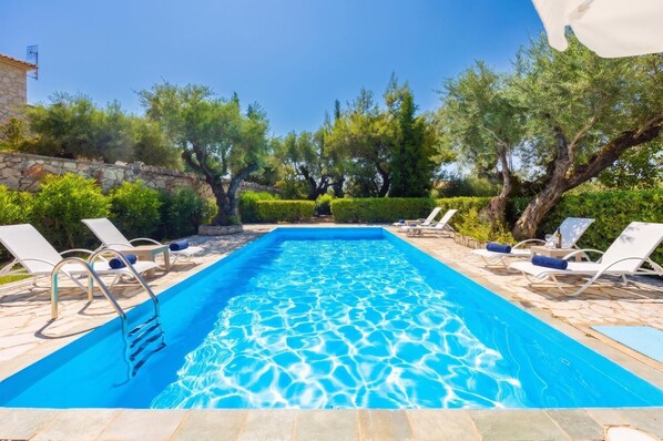 Une piscine rectangulaire à l’eau d’un bleu limpide, entourée de chaises longues et d’un dallage en pierre.